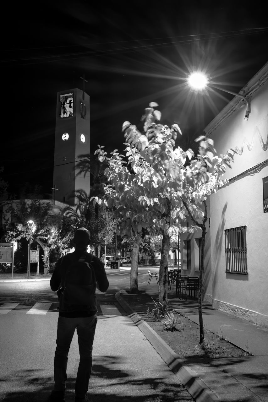 black, white, architecture, light, building exterior, lighting, night, built structure, black and white, city, darkness, one person, monochrome, street, tree, monochrome photography, road, plant, rear view, full length, nature, adult, men, illuminated, snapshot, person, clothing, standing, infrastructure, building, outdoors, lifestyles, flower