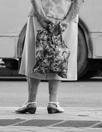 Elderly woman standing holding bag behind her back