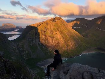 Woman sitting on rock by lake against sky during sunset