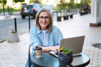 Happy and content caucasian mature woman with long grey hair, seated at street cafe with a notebook.