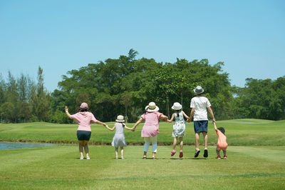 Rear view of family holding hands at park against clear blue sky