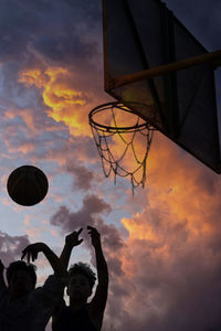 Young man with friend playing basketball during sunset