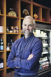 Portrait of confident mature salesman standing by rack in deli