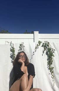 Smiling young woman against white wall against blue sky