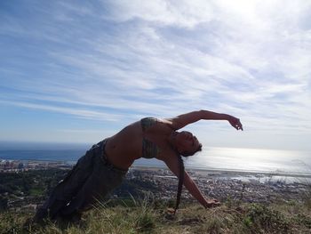 Flexible woman stretching against sky