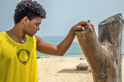 Thoughtful young man standing by bare tree against sky at beach