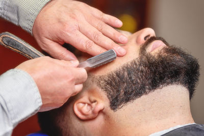 Cropped hands of barber shaving customer beard in salon