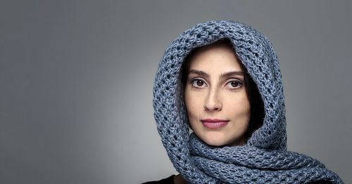 Portrait of young woman wearing headscarf against gray background