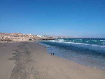 People walking at beach against clear blue sky