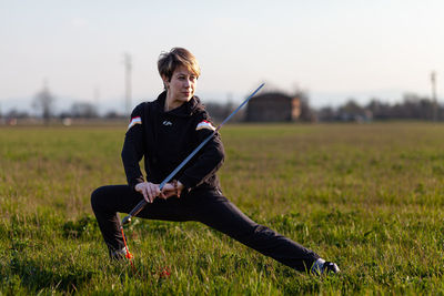 Caucasian young woman practicing wushu martial art on a green meadow with a sword