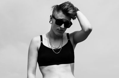 Hipster woman standing wearing sports bra against sky