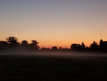 Silhouette trees on field against clear sky at sunset