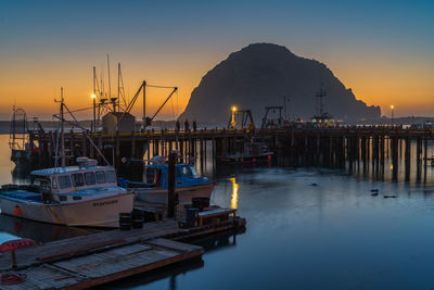 Boats moored in harbor at sunset