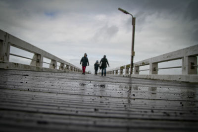 People walking on pier against cloudy sky