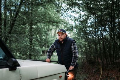 Portrait of man standing by car in forest