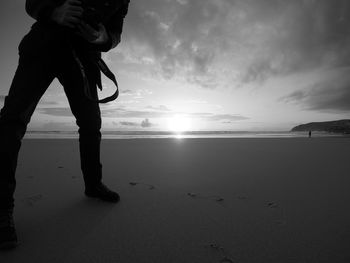 Low section of man standing on beach against sky