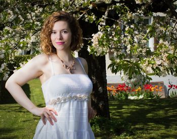 Portrait of beautiful woman in dress standing against flowering tree