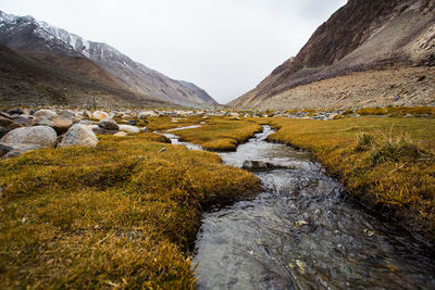 Stream flowing through rocks in river against sky