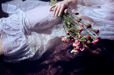 Midsection of woman holding flowers while swimming in river