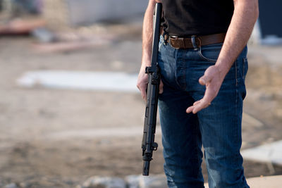 Midsection of man with rifle standing on ground