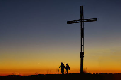 Silhouette people walking down field against sky during sunset