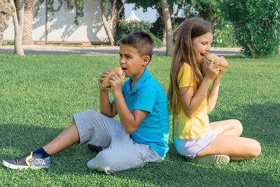 Children schoolchildren eat burgers in the park sitting on the grass. school lunch.