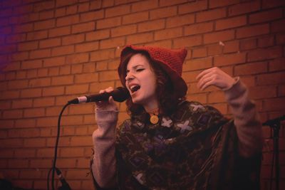 Young woman singing against brick wall