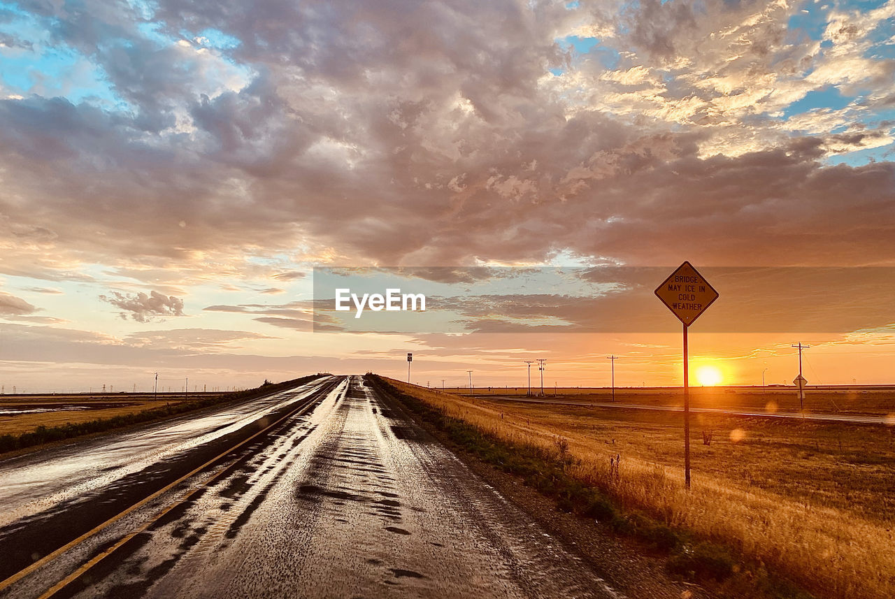 Road amidst field against sky during sunset