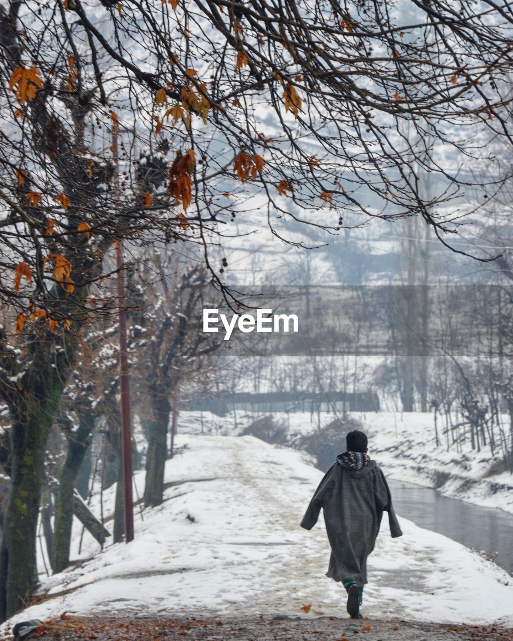 REAR VIEW OF MAN WALKING ON SNOW COVERED FIELD