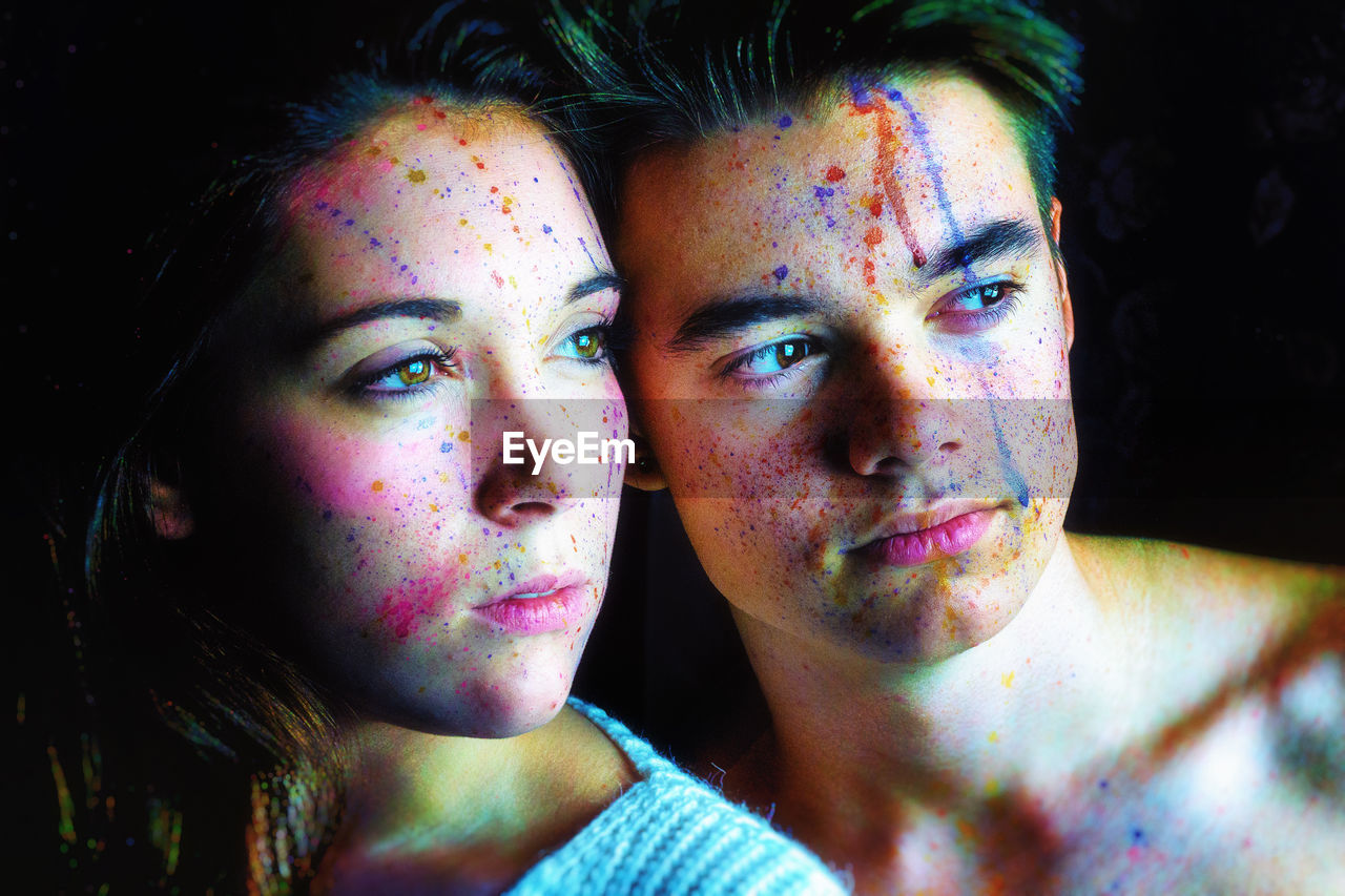 Close-up portrait of a young woman and man over black background