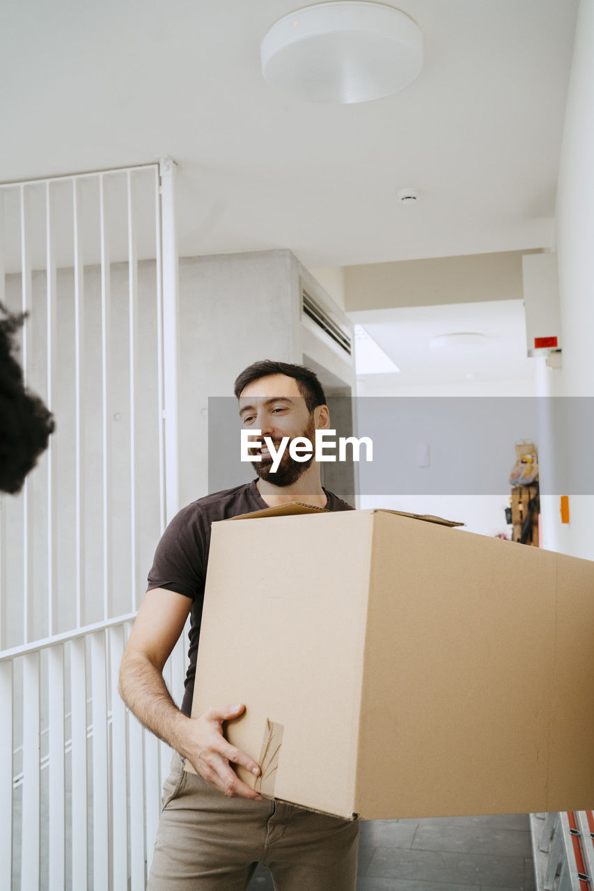 Smiling man holding cardboard box at new home