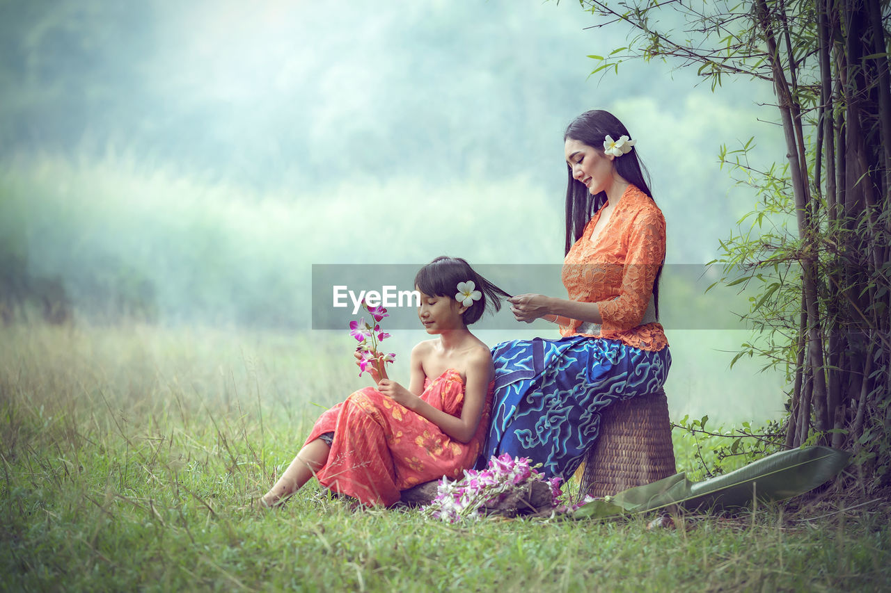 Smiling mother and daughter with flowers sitting on field