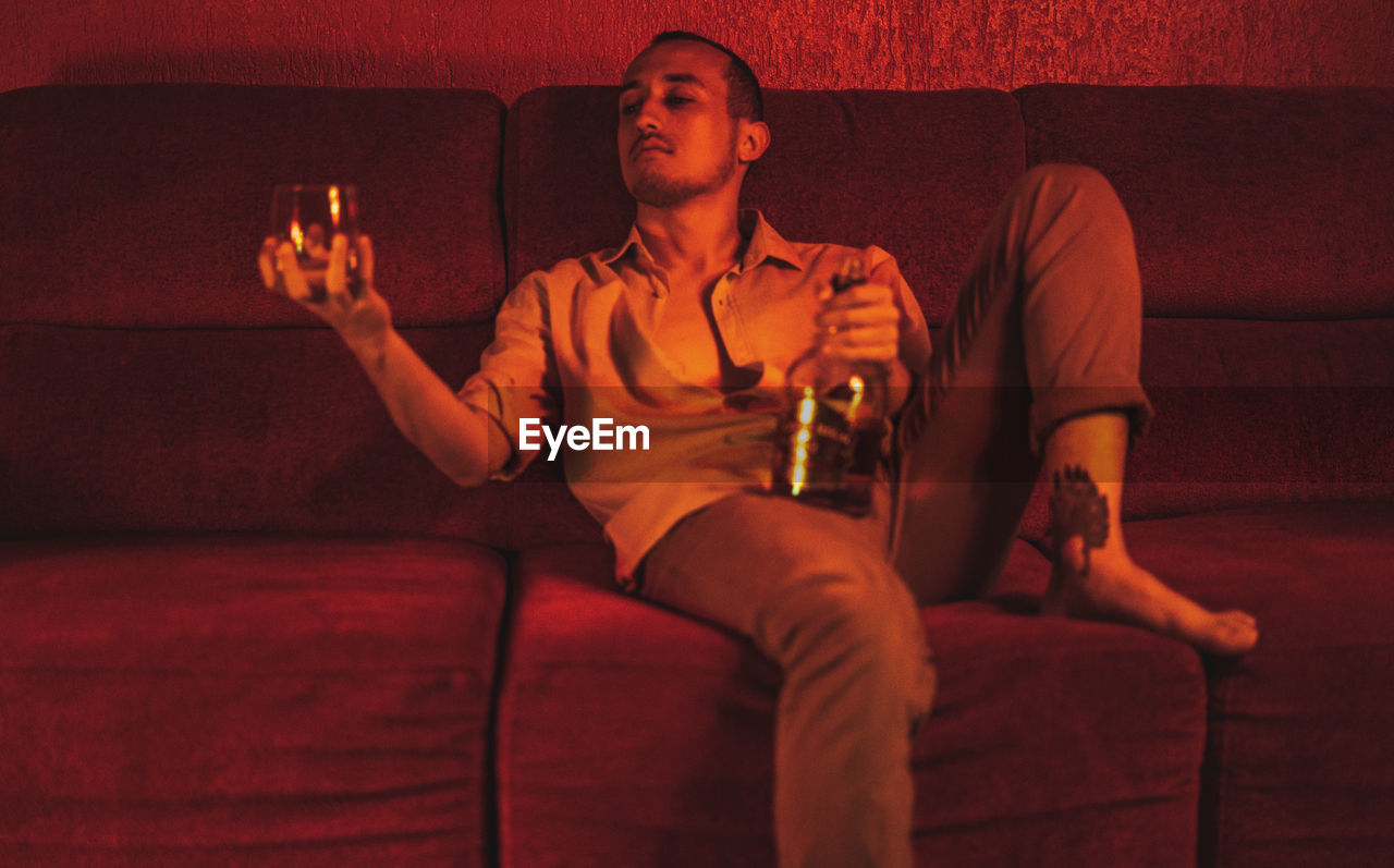 Portrait of young man drinking scotch while sitting on sofa at home