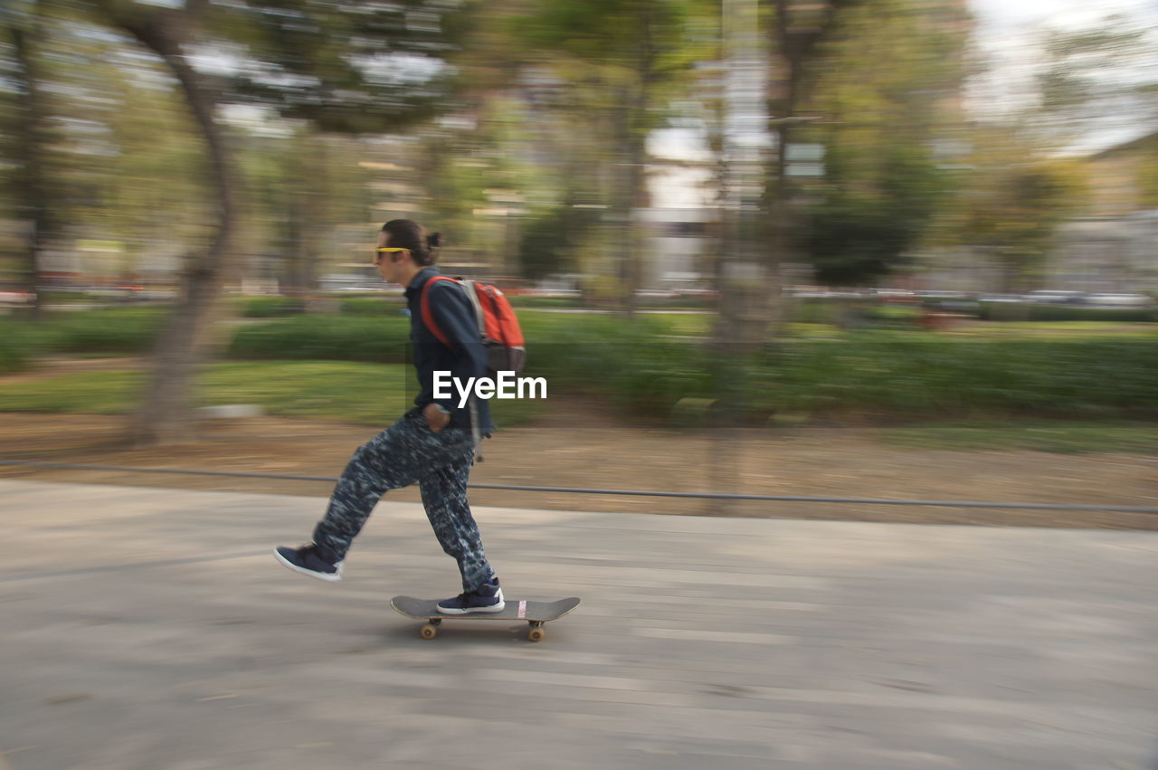 FULL LENGTH OF A MAN SKATEBOARDING ON ROAD