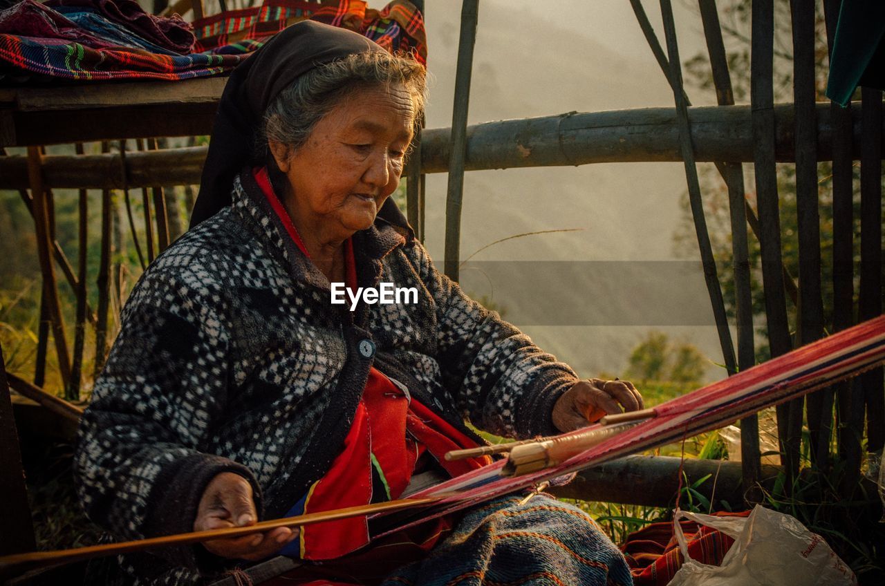 Senior woman weaving while sitting outdoors