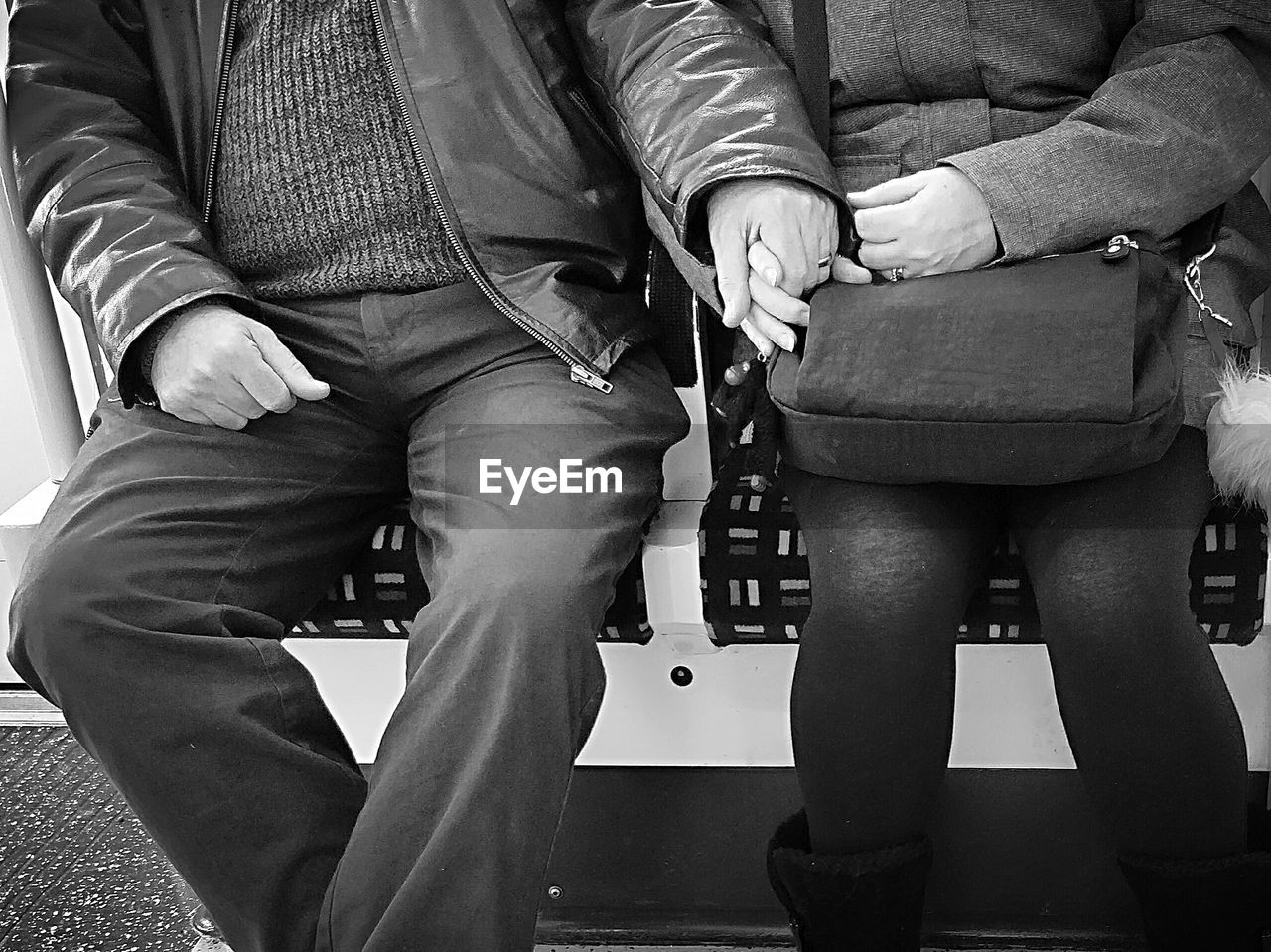 Midsection of couple holding hands while sitting in metro train