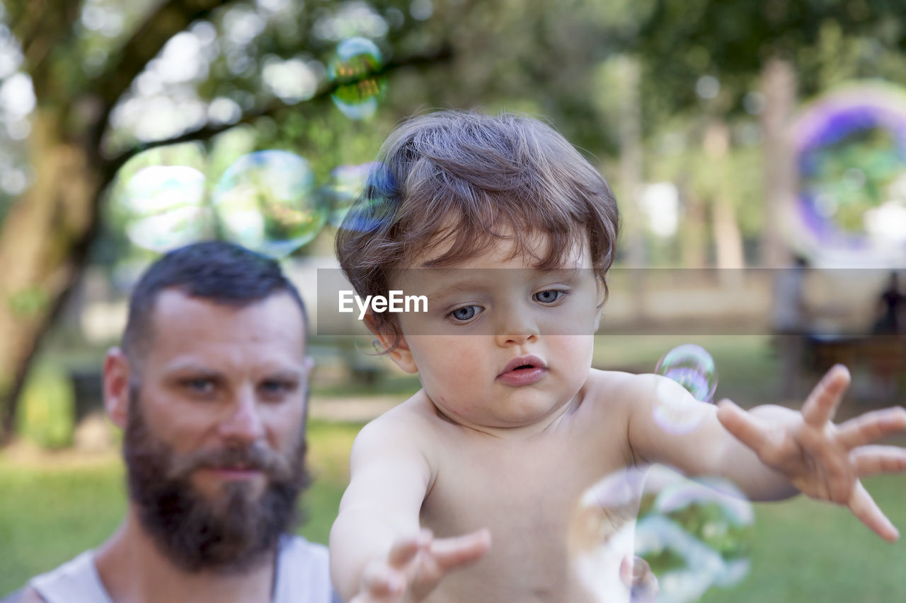 Portrait of father by son playing with bubbles in park