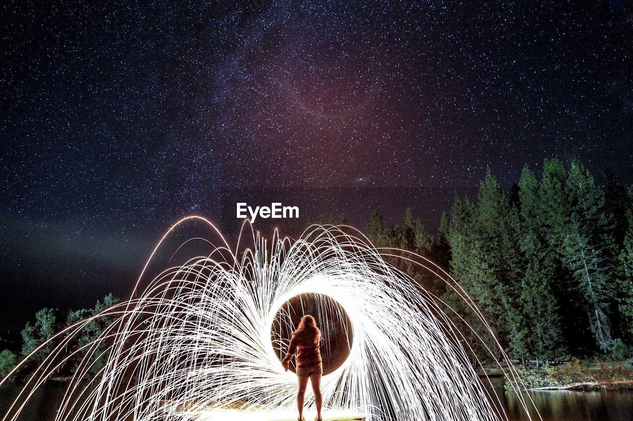 Rear view of woman with wire wool on pier over lake at night