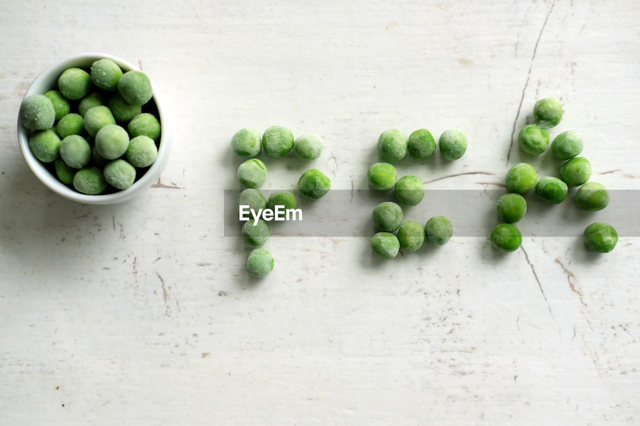 Frozen green peas in a bowl on white rustic wooden board - top view