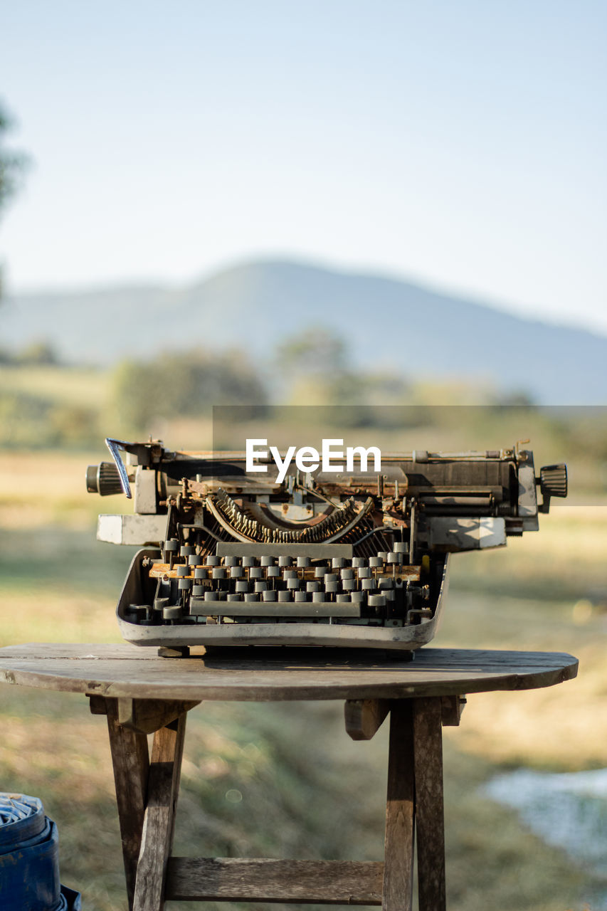 An old typewriter on a wooden table there is a rice field in the background.