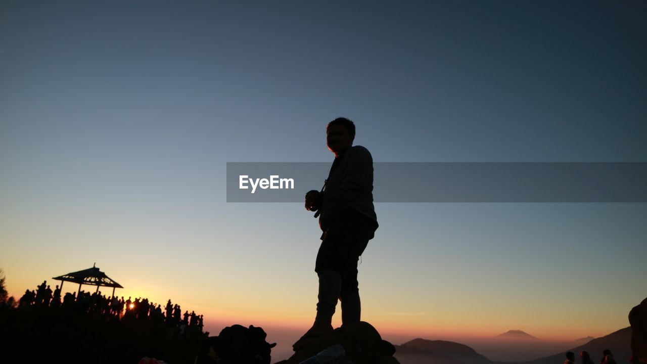 low angle view of silhouette man standing on mountain against sky during sunset