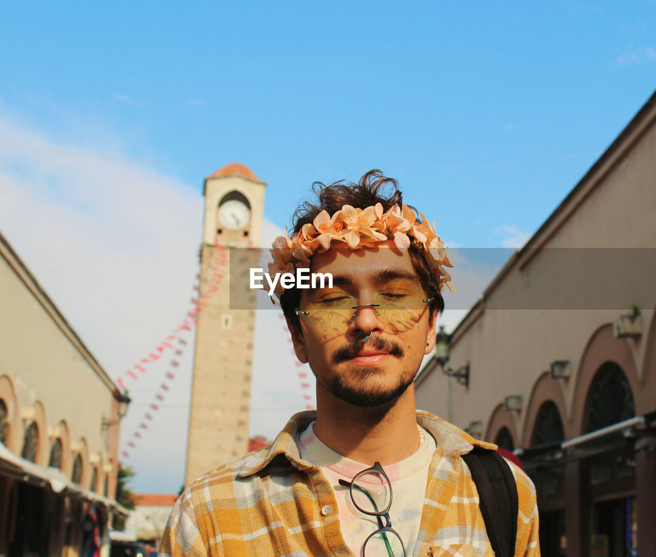 Portrait of young man with eye makeup and flower crown behind historic old clock tower adana turkey