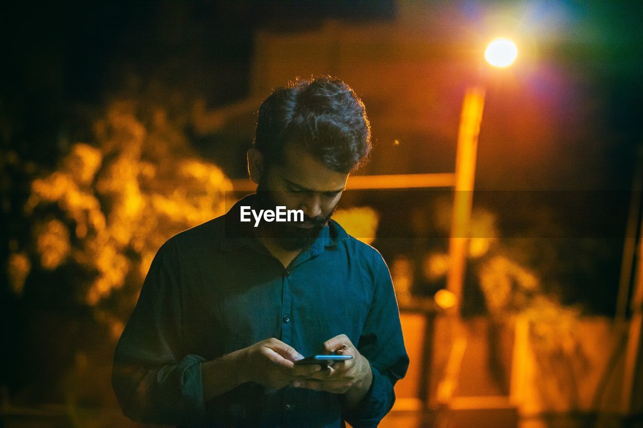 Young man using smart phone on street at night
