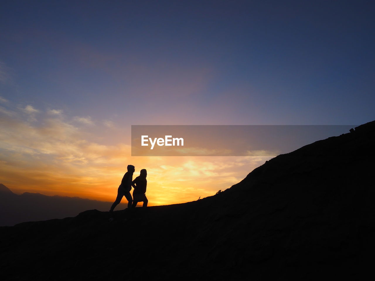 Silhouette men standing on mountain against sky during sunrise
