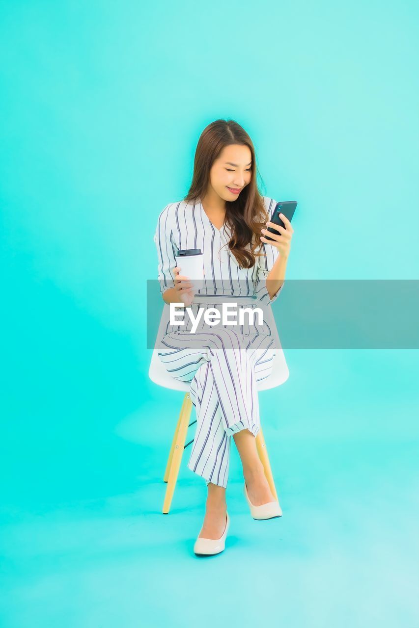 YOUNG WOMAN USING PHONE AGAINST BLUE BACKGROUND