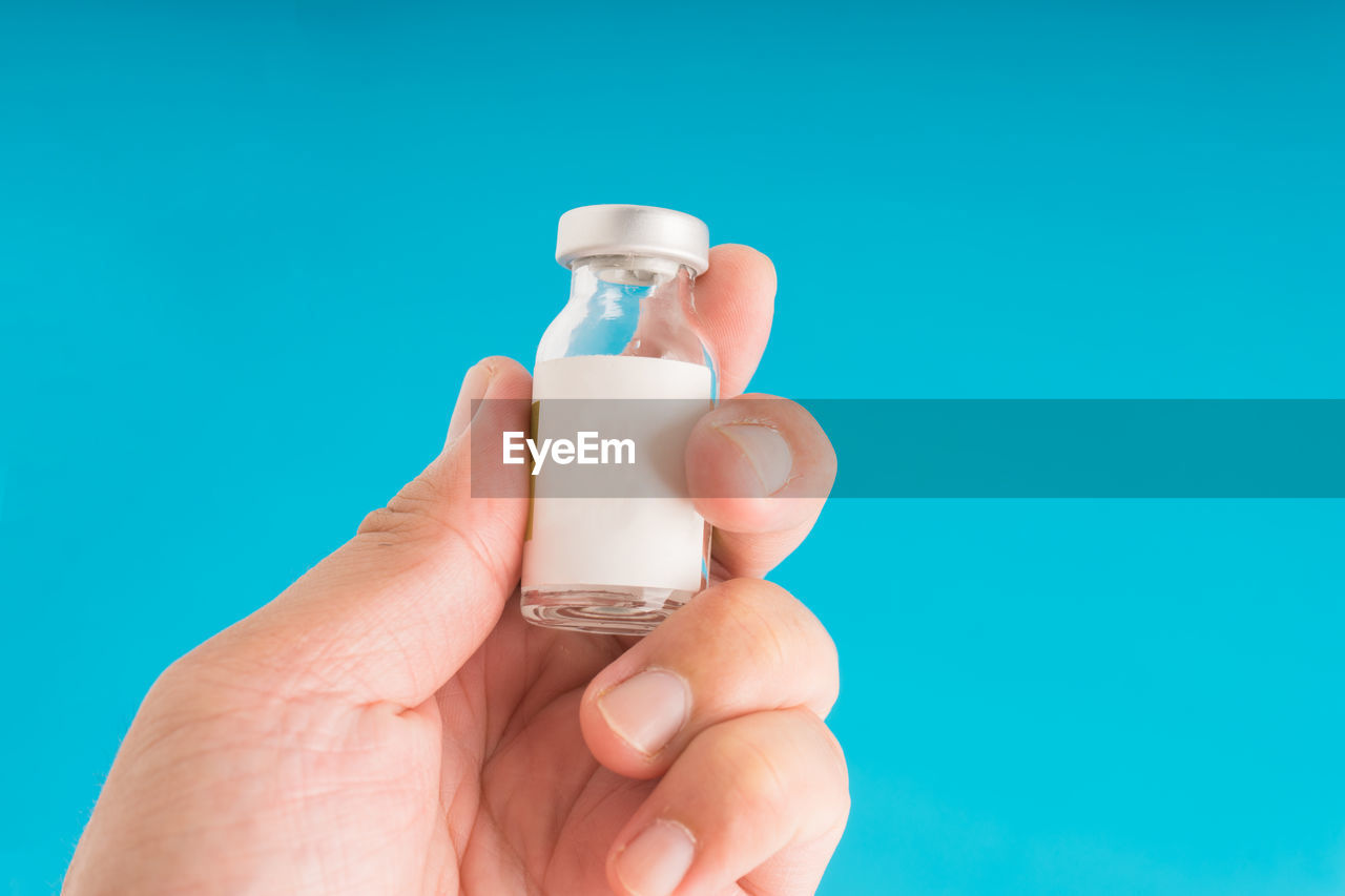 Cropped hand of person holding vial against blue background