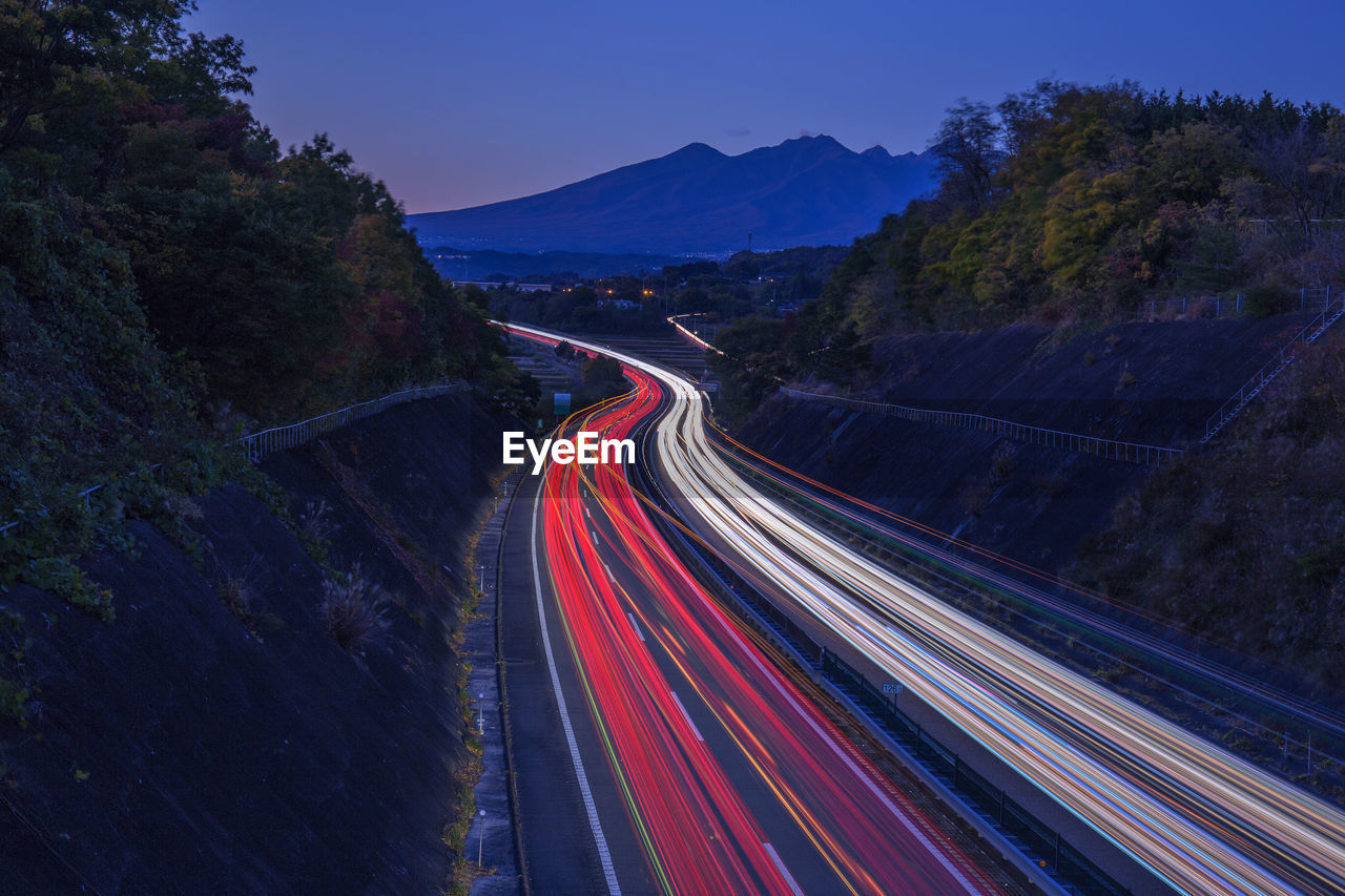 Light trails on road by mountain against sky at night