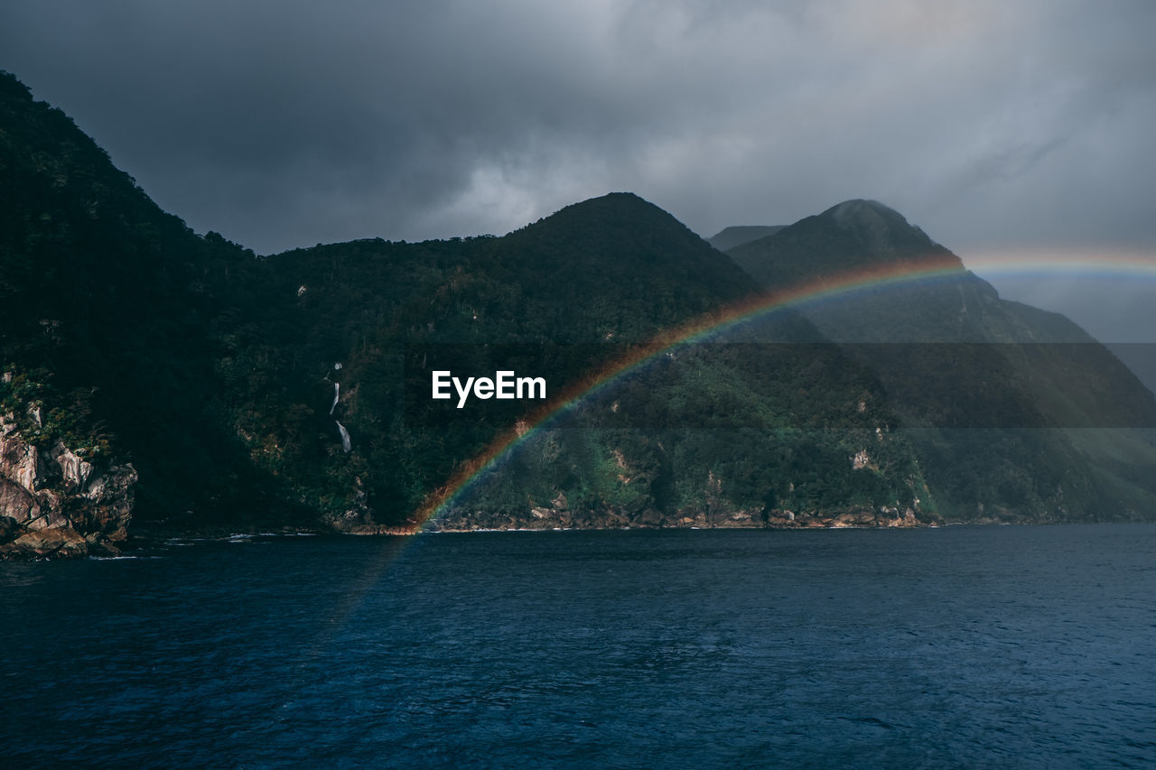 Scenic view of rainbow over sea and mountains