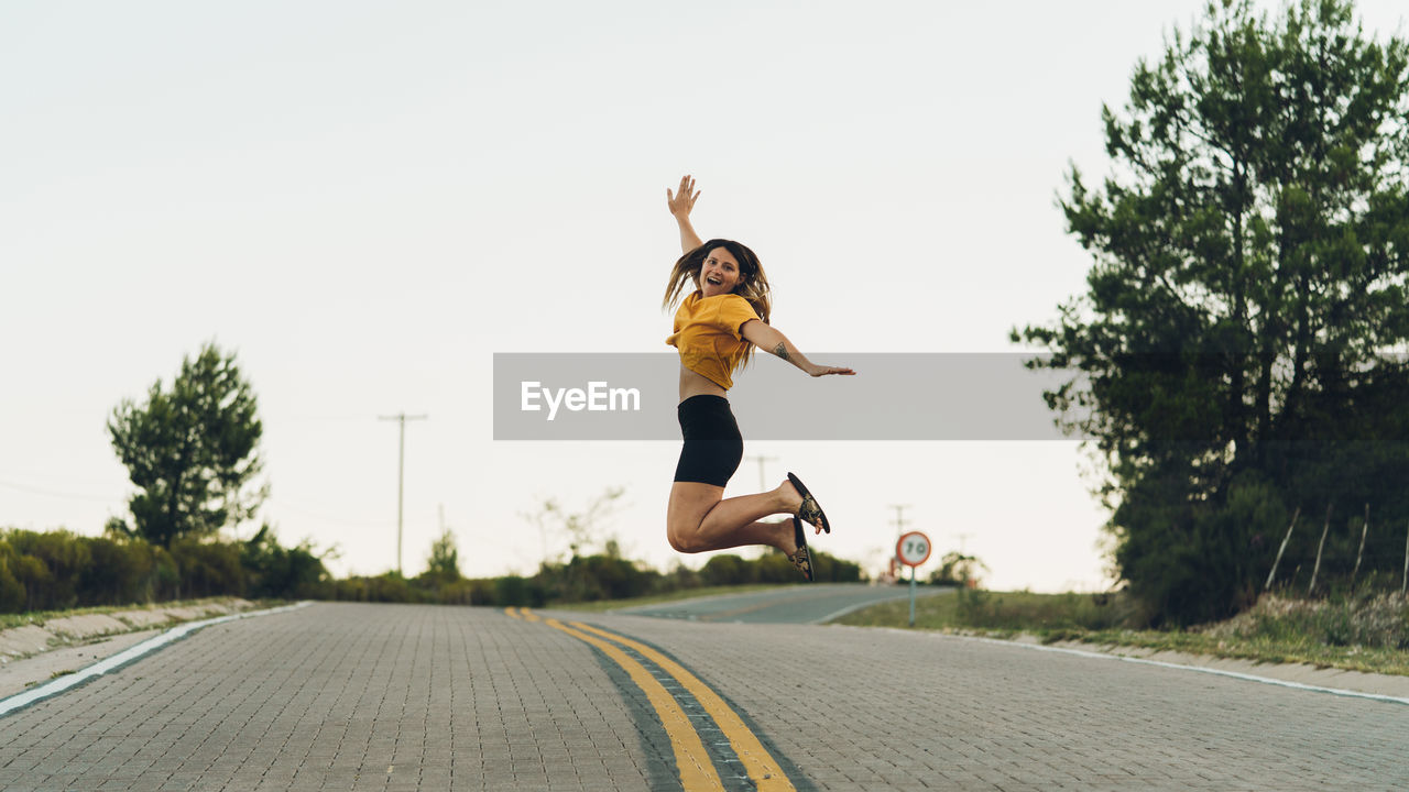 Young woman jumping on road against clear sky