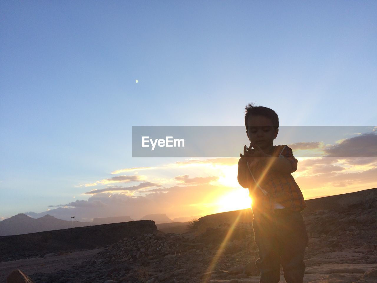 BOY STANDING AT SUNSET AGAINST SKY